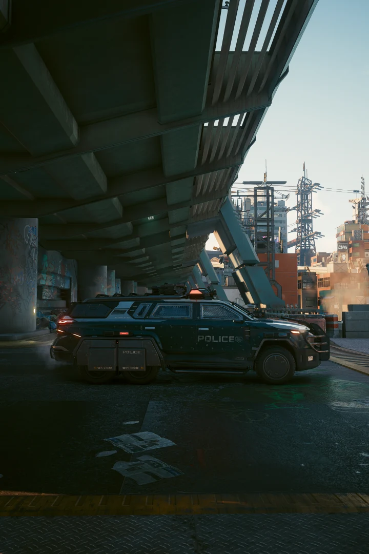 A Thorton Merrimac, POLICE on its door, parked in the shade under an overpass, late light on the buildings and pylons beyond