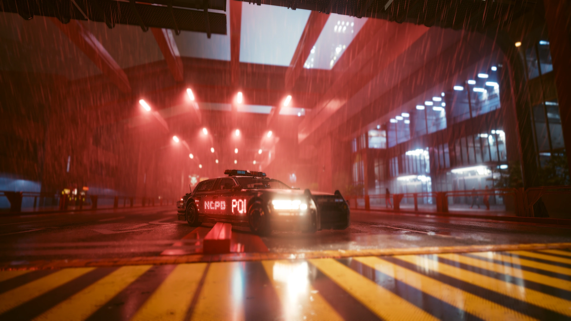 A patrol car with its headlights on under a red-lit overpass in the rain, yellow hazard stripes in the foreground